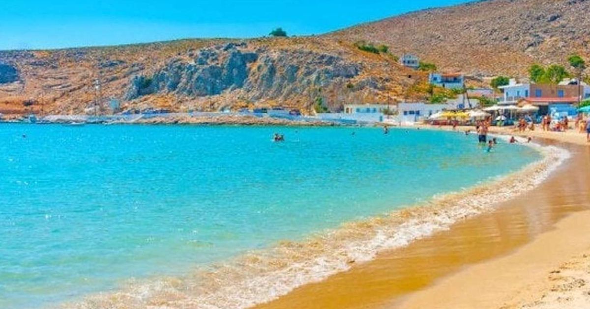 Sandy beach and turquoise bay with a small village on the hillside, a swim stop on the island cruise route