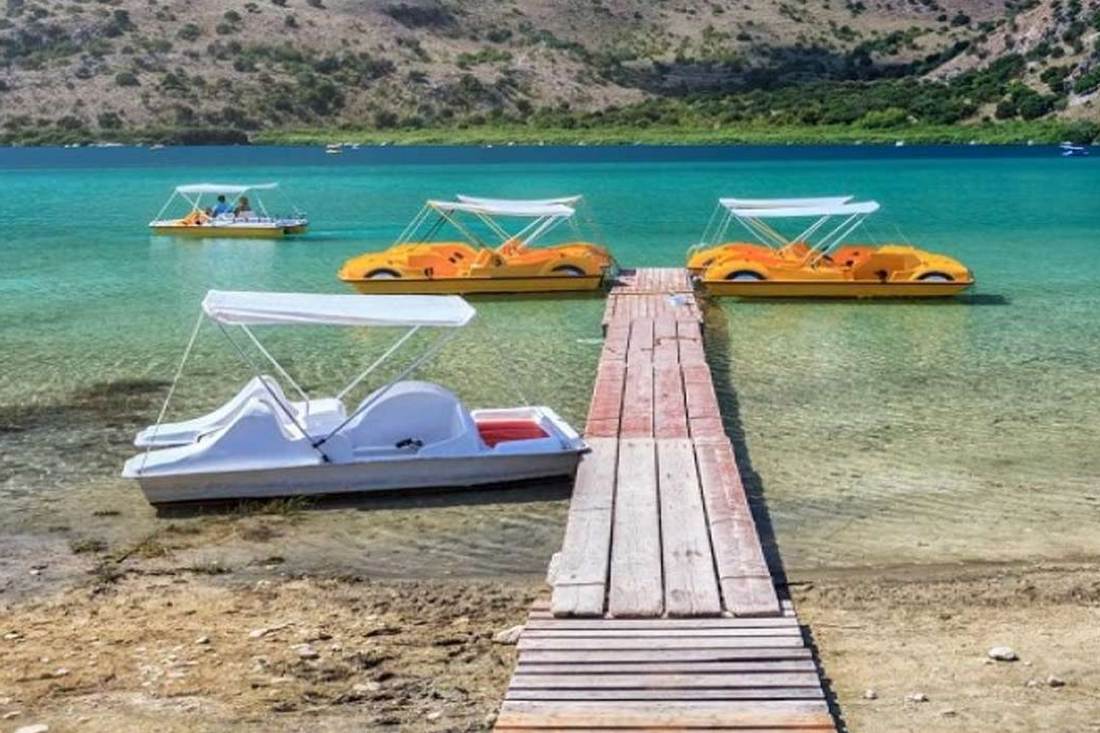 Yellow and white pedal boats moored beside a wooden jetty on the clear water of Lake Kournas.