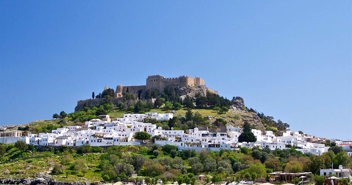The Acropolis of Lindos, a walled fortress on a hill above the white village houses, under a clear blue sky