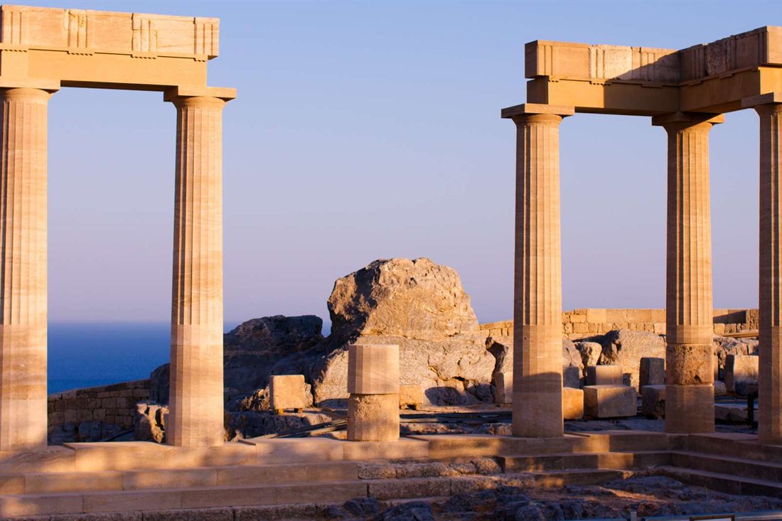 Ancient Doric columns on the Lindos acropolis with the blue sea beyond them.