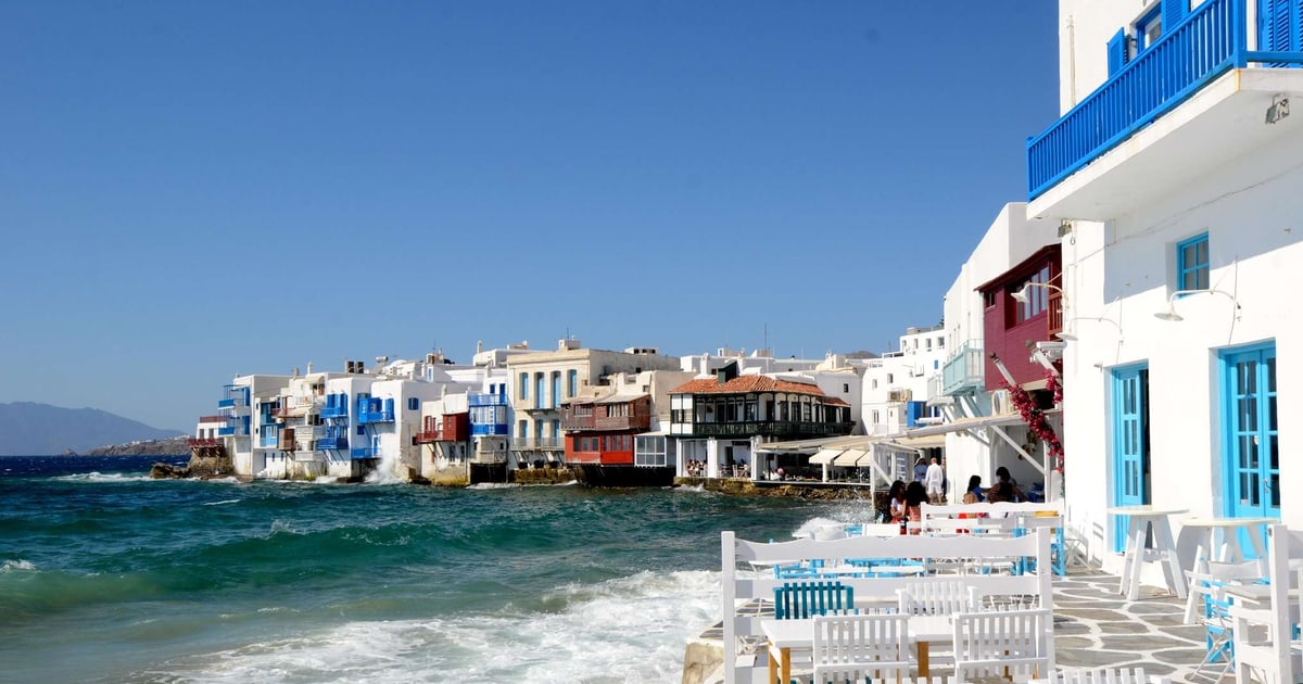 Whitewashed waterfront houses with blue balconies at Little Venice, Mykonos, above a turquoise sea.